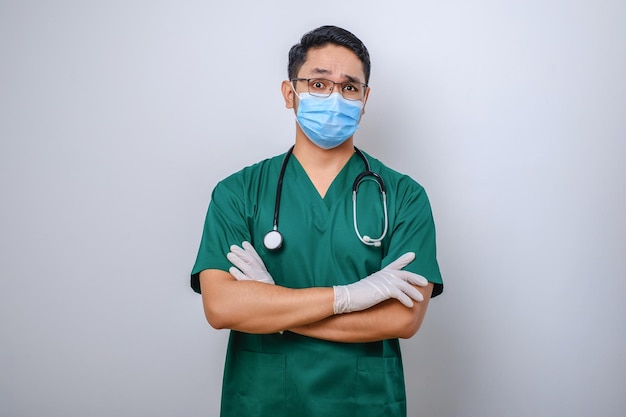 Professionele, serieus ogende aziatische arts-medische werker in stethoscoop en scrubs met een medisch masker dat kruisarmen doet