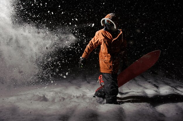 Professionele snowboarder in oranje sportkleding met een bord 's nachts