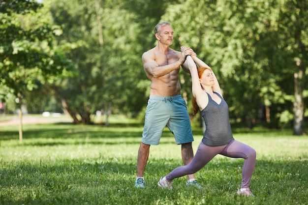 Professionele spiergebonden trainer yoga pose van de vrouw aan te passen terwijl ze oefenen in zomer park