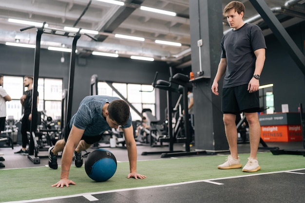 Foto professionele sportcoach legt een beginnende sportman uit hoe hij met een zware fitnessbal moet trainen