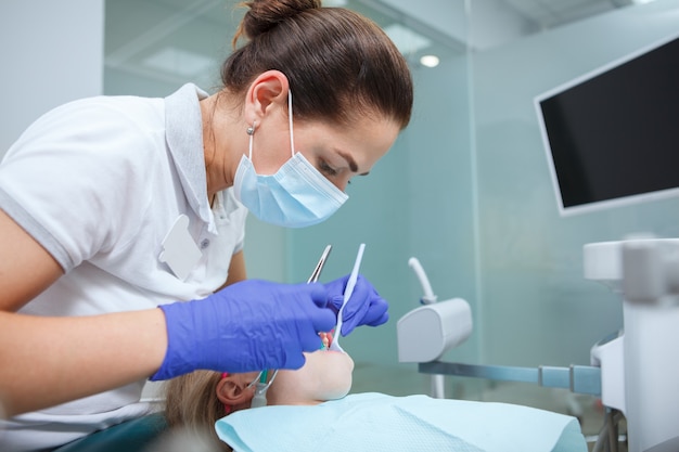 Professionele tandarts die in haar tandheelkundige kliniek werkt en de tanden van een kind behandelt