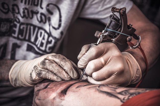 Professionele tatoeëerder die de tatoeage verbrandt met handschoenen aan door een speciale gereedschapsclose-up.