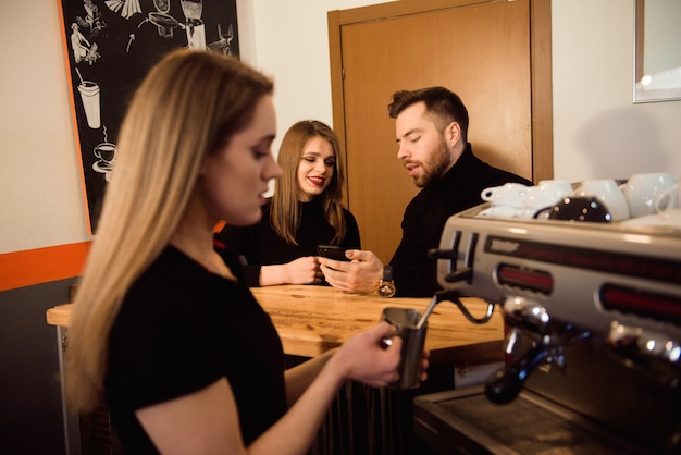 Professionele vrouwelijke barista houden metalen kruik verwarmende melk met behulp van de koffiemachine.