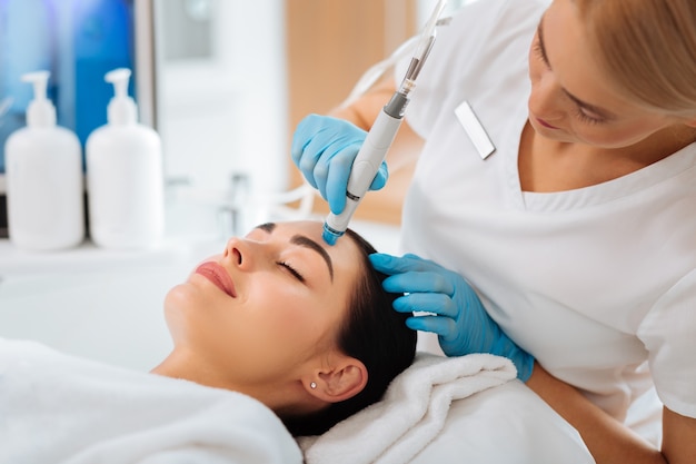 Professionele vrouwelijke cosmetoloog die een hydrafaciale ingreep doet terwijl ze aan het werk is