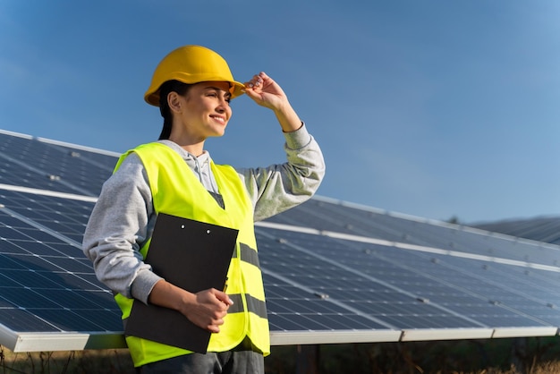 Professionele vrouwelijke ingenieur die wegkijkt met plezierglimlach terwijl hij werkt aan een ecologisch groen veld met zonnepanelen Fotovoltaïsche krachtcentraleconcept