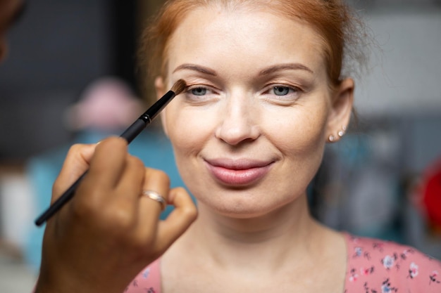 Professionele vrouwelijke make-upartiest die cosmetica aanbrengt op het gezicht van een zwangere vrouw, gebruikt een borstel die bij be...