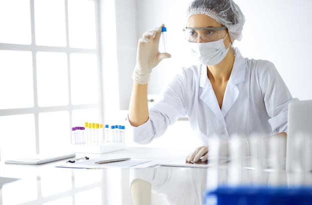 Professionele vrouwelijke wetenschapper in beschermende brillen die buis met reagentia in laboratorium onderzoeken. Concepten van geneeskunde en onderzoek.