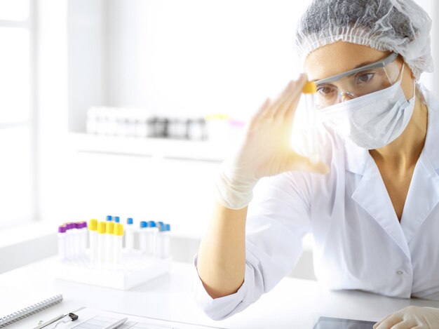 Professionele vrouwelijke wetenschapper in beschermende brillen die buis met reagentia in zonnig laboratorium onderzoeken. Geneeskunde en onderzoek.