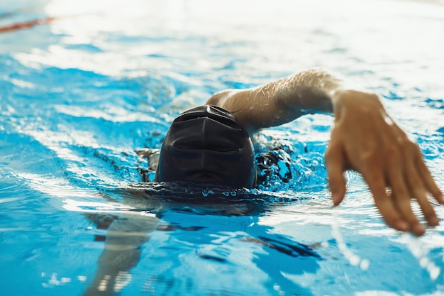 Professionele vrouwelijke zwemmer in pet die een kruipslag doet tijdens het freestyle zwemmen in het binnenzwembad