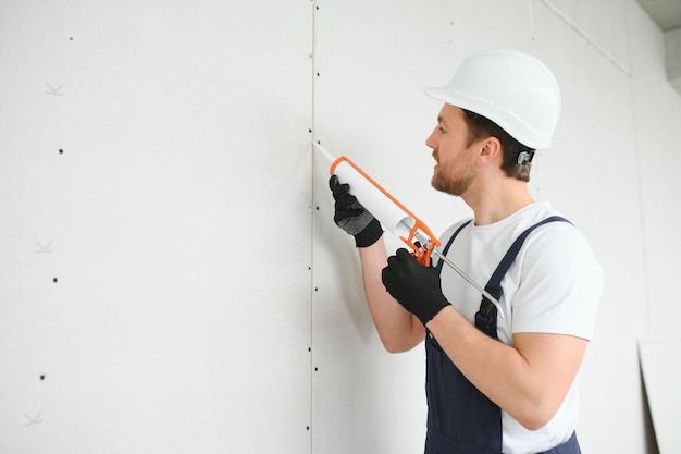 Professionele werkman die siliconenkit aanbrengt met een kitpistool op de muur