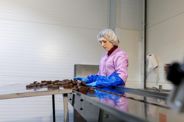 Professionele werkneemster in uniform en beschermende handschoenen sorteert chocoladesuikergoed op de productielijn in de fabriek