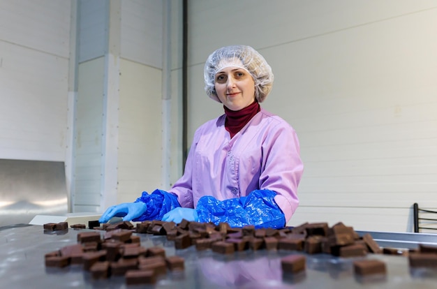 Professionele werkneemster in uniform en beschermende handschoenen sorteert chocoladesuikergoed op de productielijn in de fabriek
