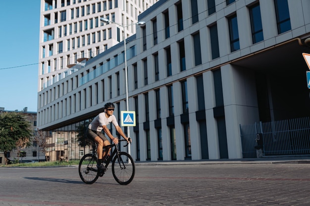 Professionele wielrenner in veiligheidshelm en gespiegelde bril die buiten fietst Blanke man met gespierde benen die alleen op straat in de stad traint