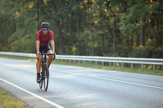 Professionele wielrenner zwarte fiets rijden op asfaltweg tussen de groene natuur.