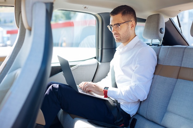 Foto professionele zakenman. slimme succesvolle zakenman met behulp van zijn laptop tijdens het werken vanuit de auto