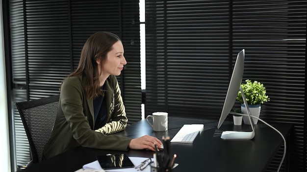 Professionele zakenvrouw die de financiële markt op het computerscherm analyseert terwijl ze in een modern kantoor zit
