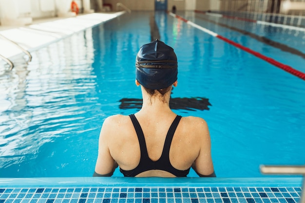 Professionele zwemster in pet en zwembroek die tijdens de training op de baan in het zwembad staat