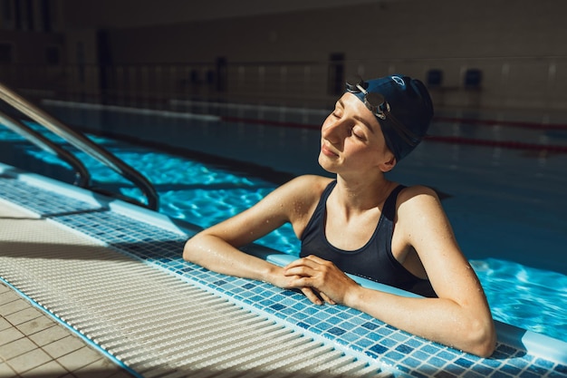 Professionele zwemster leunend op de rand van het zwembad en genietend van zonlicht met gesloten ogen