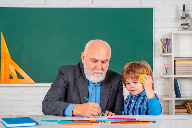 Professore e allievo in aula presso la scuola elementare bambino a scuola lezione con insegnante senior studente a scuola con insegnante anziano