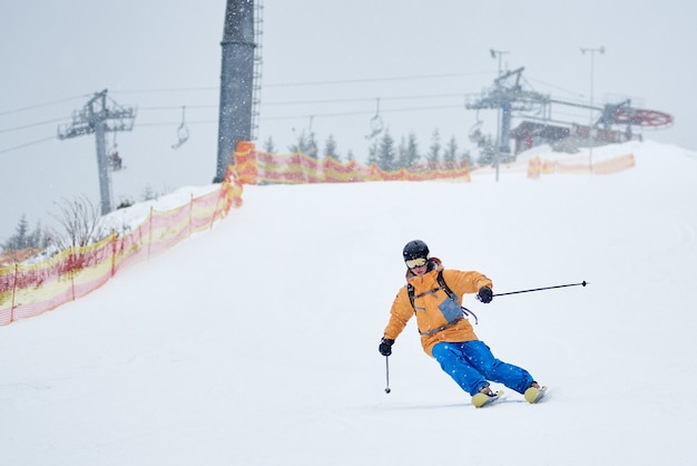 Proficient male skier skiing in snowfall downhill from snow-covered slope with net on edge