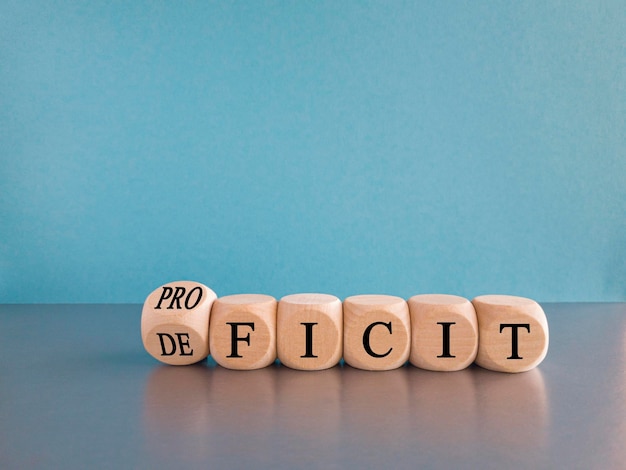 Photo proficit or deficit symbol turned wooden cube and changes the concept word deficit to proficit