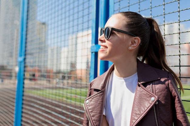 Profiel close-up portret van stijlvolle mooie dame met verzameld golvend kapsel met zonnebril wit overhemd en jas kijkt omhoog en geniet van warme lentedag