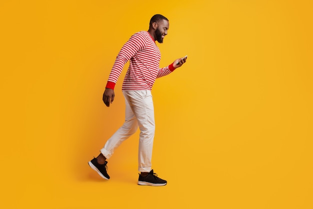 Profiel portret van man houdt smartphone kijk scherm lopen op gele achtergrond