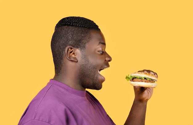 Profiel portret van zwarte man hamburger eten op gele achtergrond