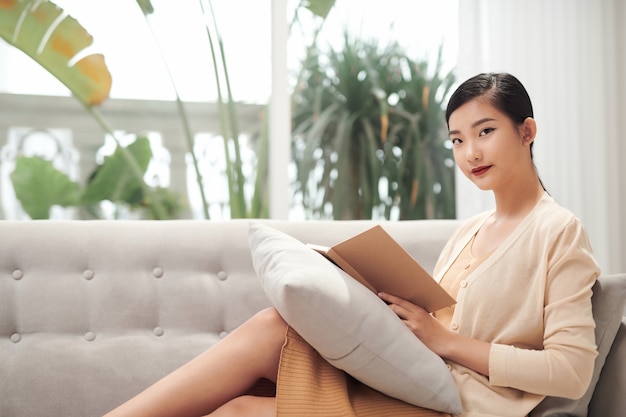 Profiel van een jonge aziatische vrouw die op de bank ontspant en thuis een nieuw boek leest