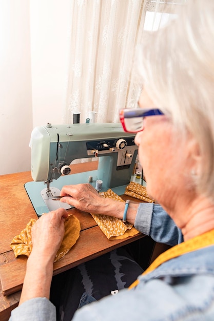 Profiel van een oudere vrouw voor een antieke naaimachine die een draad van een oranje stof snijdt