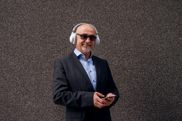 Profiel van een volwassen vrolijke professionele elegante zakenman luistert naar muziek op de telefoon met een koptelefoon.