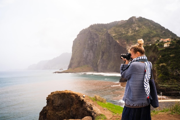 Profiel van een vrouw in sjaal die foto's maakt met een digitale camera van de zee