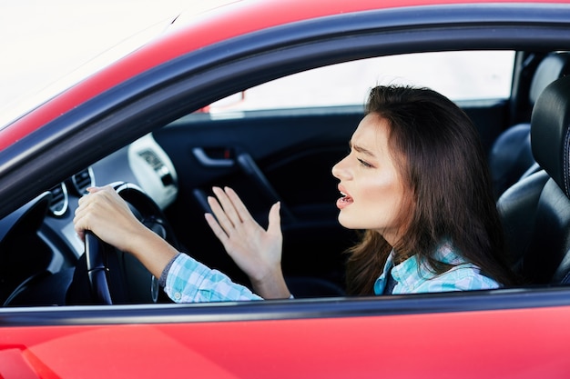 Profiel van :: gestrest vrouw rode auto rijden, stress tijdens het rijden. Vrouw die zenuwachtig vooruit kijkt, files. Hoofd en schouders van brunette vrouw in auto