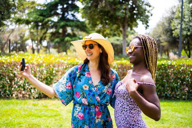 Profiel van multi-etnische vrouwen in zomerjurk die glimlachen terwijl ze een selfie maken in een tuin