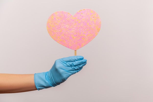 Profiel zijaanzicht close-up van menselijke hand in blauwe chirurgische handschoenen met hart roze liefdesstok.