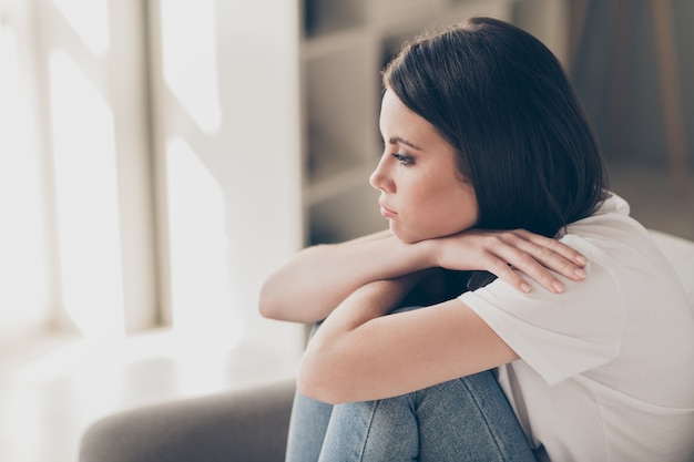 Profielfoto aan de zijkant van een aantrekkelijk jong meisje, alledaagse problemen, denkconcept, zit binnenshuis op de bank