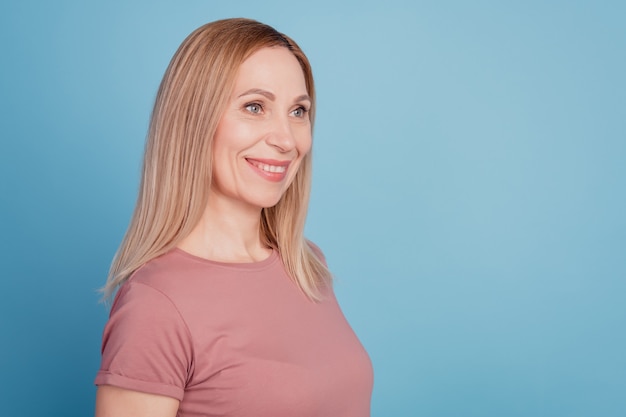 Profielfoto aan de zijkant van een jonge, aantrekkelijke vrouw die een gelukkig positief glimlach draagt en een t-shirt draagt dat over een blauwe kleurachtergrond wordt geïsoleerd
