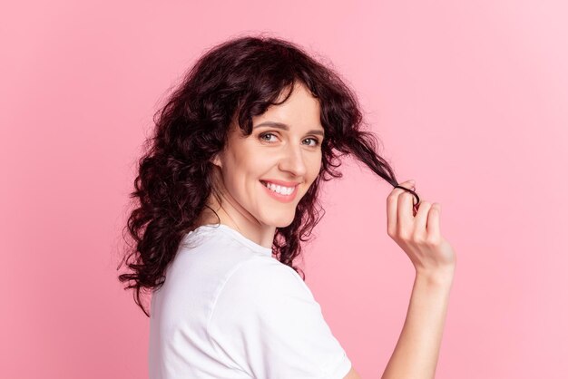 Profielfoto aan de zijkant van een jonge schattige vrouw die haar nieuwskapsel met de hand aanraakt, geïsoleerd over een roze kleurachtergrond