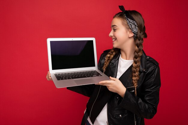 Profielfoto aan de zijkant van een mooi gelukkig lachend meisje met donkerbruine staartjes die een computerlaptop vasthouden