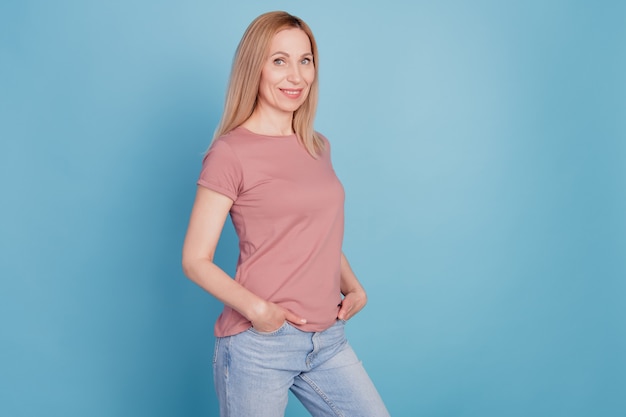 Profielfoto aan de zijkant van een vrolijke positieve schattige aardige jonge vrouw handen in zak casual outfit geïsoleerde blauwe kleur achtergrond