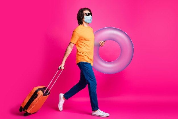 Profielfoto over de volledige lengte van kerel go hold case rubberen cirkel draag t-shirt jeans medisch masker geïsoleerd roze kleur achtergrond