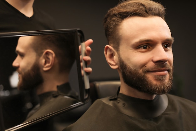 Profielfoto van een jonge kapper die het haar van zijn klant trimt met een elektrisch scheerapparaat en een kam in een kapperszaak.