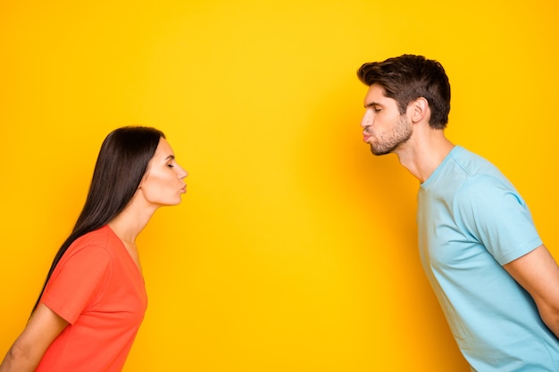 Profielfoto van grappige schattige twee mensen man dame ogen gesloten staande tegenover blinde kussen dating slijtage casual blauw oranje t-shirts geïsoleerde gele kleur muur