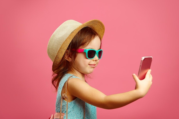 Profielfoto van klein meisje maakt een selfie-portret aan de telefoon, gekleed in zomerjurk