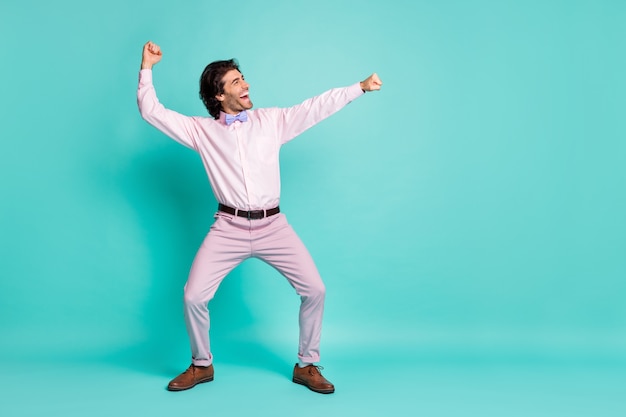 Profielfoto van vrolijke brunet krullend haar clubber man draagt roze shirt dansen uitrekkende vuisten kant kijken lege ruimte geïsoleerde groenblauw kleur achtergrond