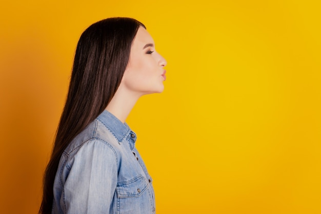 Profielportret van een charmante schattige vrouw die luchtkus op gele achtergrond verzendt