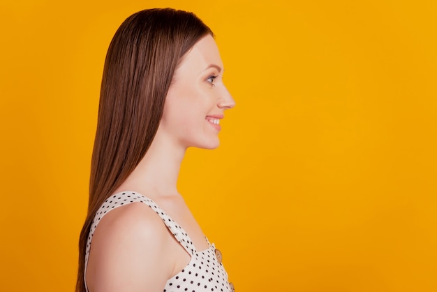 Profielportret van een vrolijke, verbluffende brunette dame ziet er lege ruimte uit met een stralende glimlach op gele achtergrond