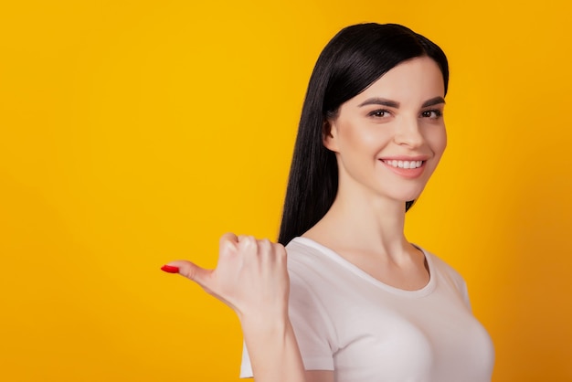 Profielzijfoto van een vrolijk jong meisje wijst duim lege ruimte reclame promo geïsoleerd over gele kleur achtergrond