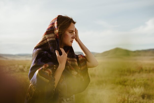 Profile of a girl correcting her cape on her head against the background of steppe grass