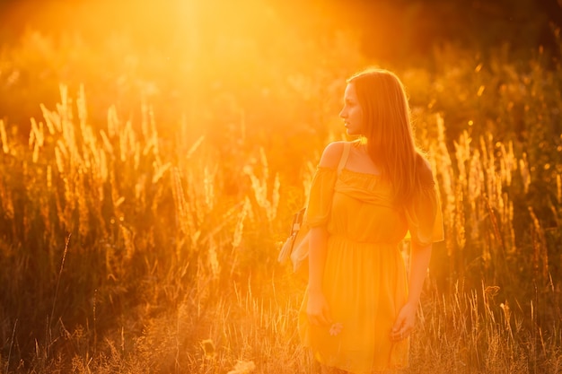 profile of a girl in a yellow dress and a backpack on her shoulder on sunset